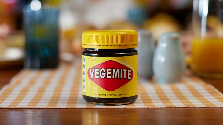Jar of Vegemite on wooden kitchen table with background blurred. 