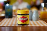 Jar of Vegemite on wooden kitchen table with background blurred. 