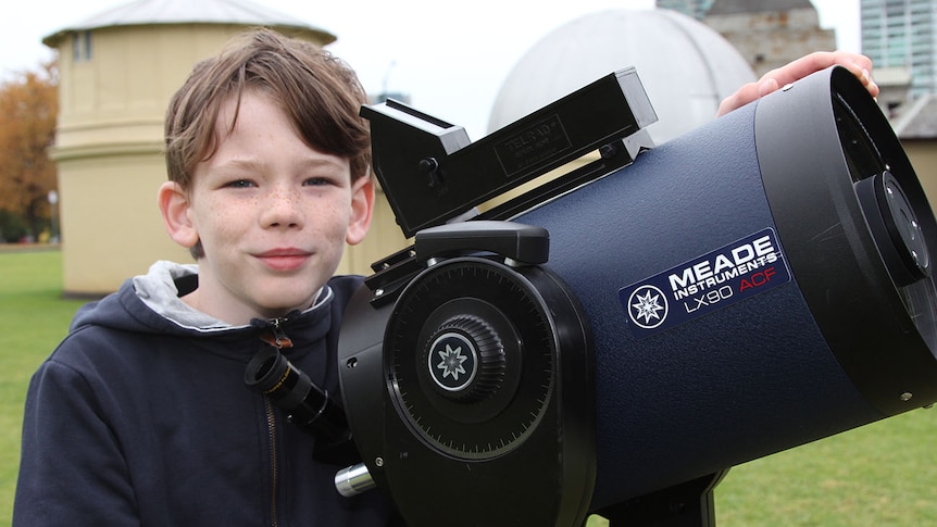 An 11-year-old boy smiling with a large blue telescope.