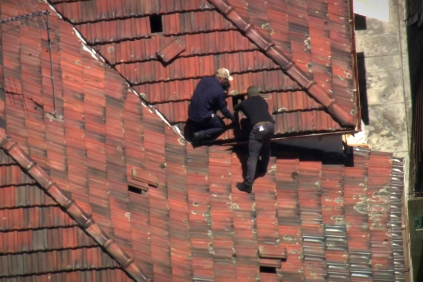 Two men on the roof of a home pulling up tiles
