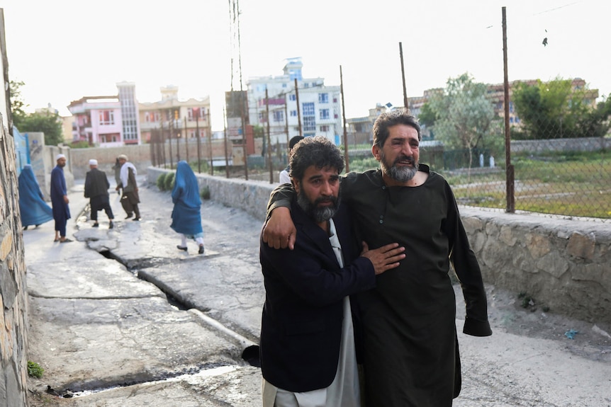 Two men lean on each other as they flee down a street.