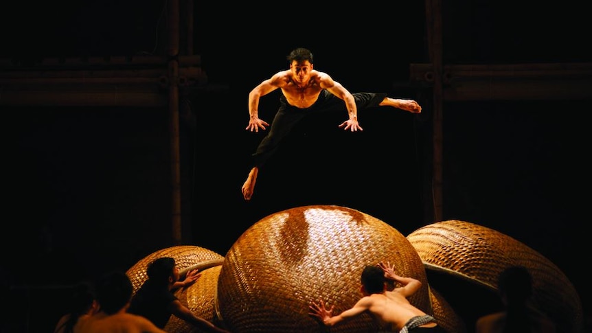 A male acrobat leaps over a huge woven orb.