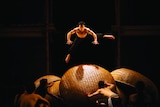 A male acrobat leaps over a huge woven orb.