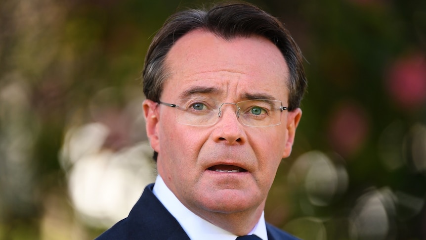 Michael O'Brien, dressed in a suit and blue tie, stands in a park.