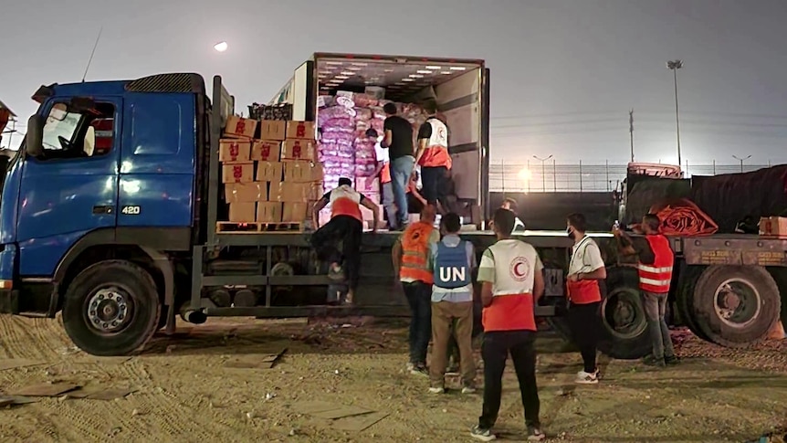 People wearing various uniforms, one saying UN, standing in front of a truck with boxes on board
