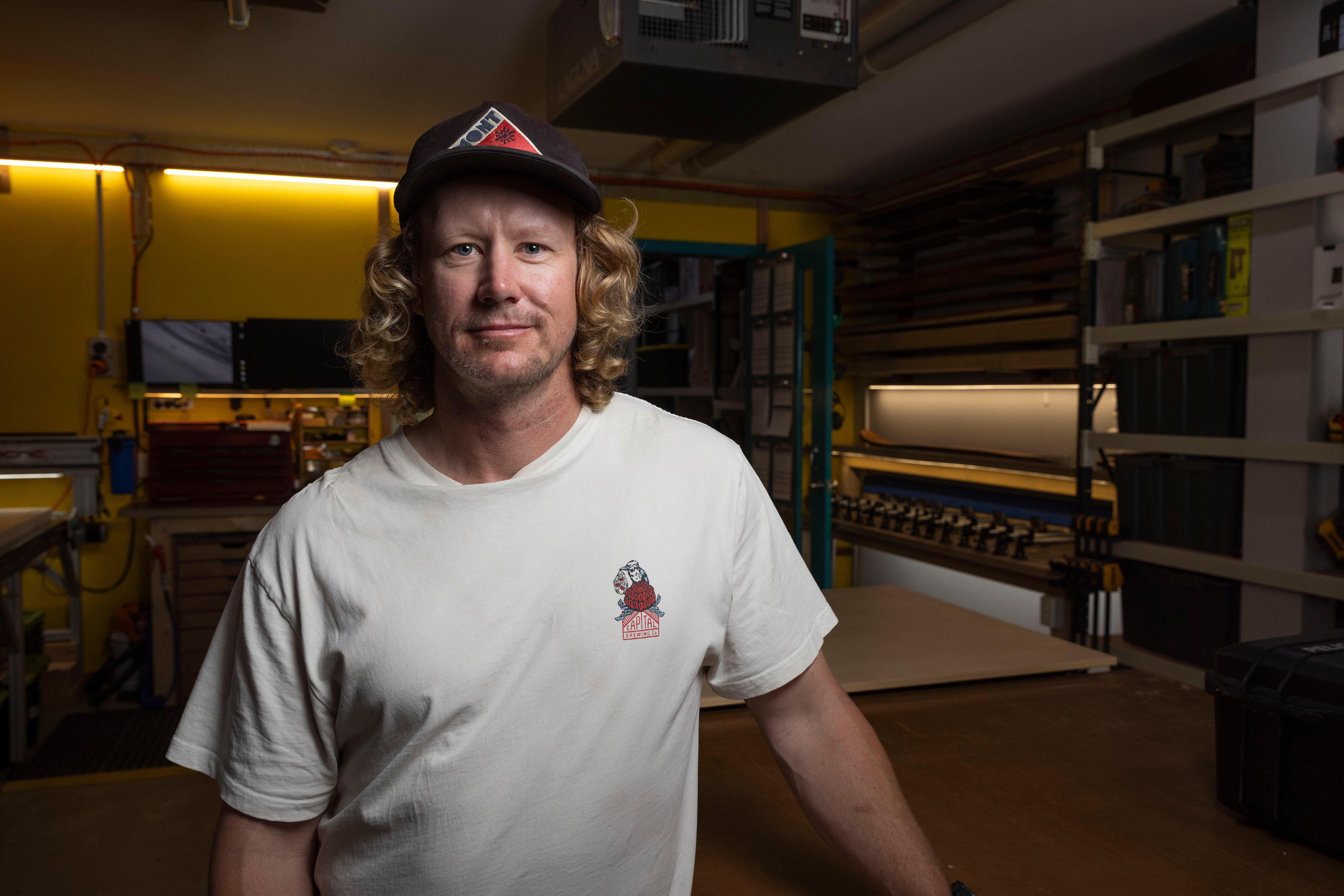 A man in a shirt and hat, standing in a workshop.