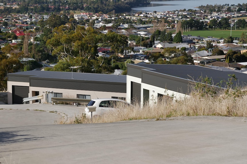 Side view of white oblong house with flat grey roof, views over suburbs, grey concrete driveway 