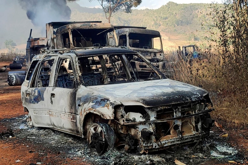 Burnt out vehicles smolder in grassland.