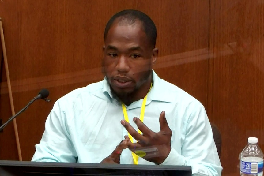 A young black man in a light green shirt makes a point, seated in a courtroom.