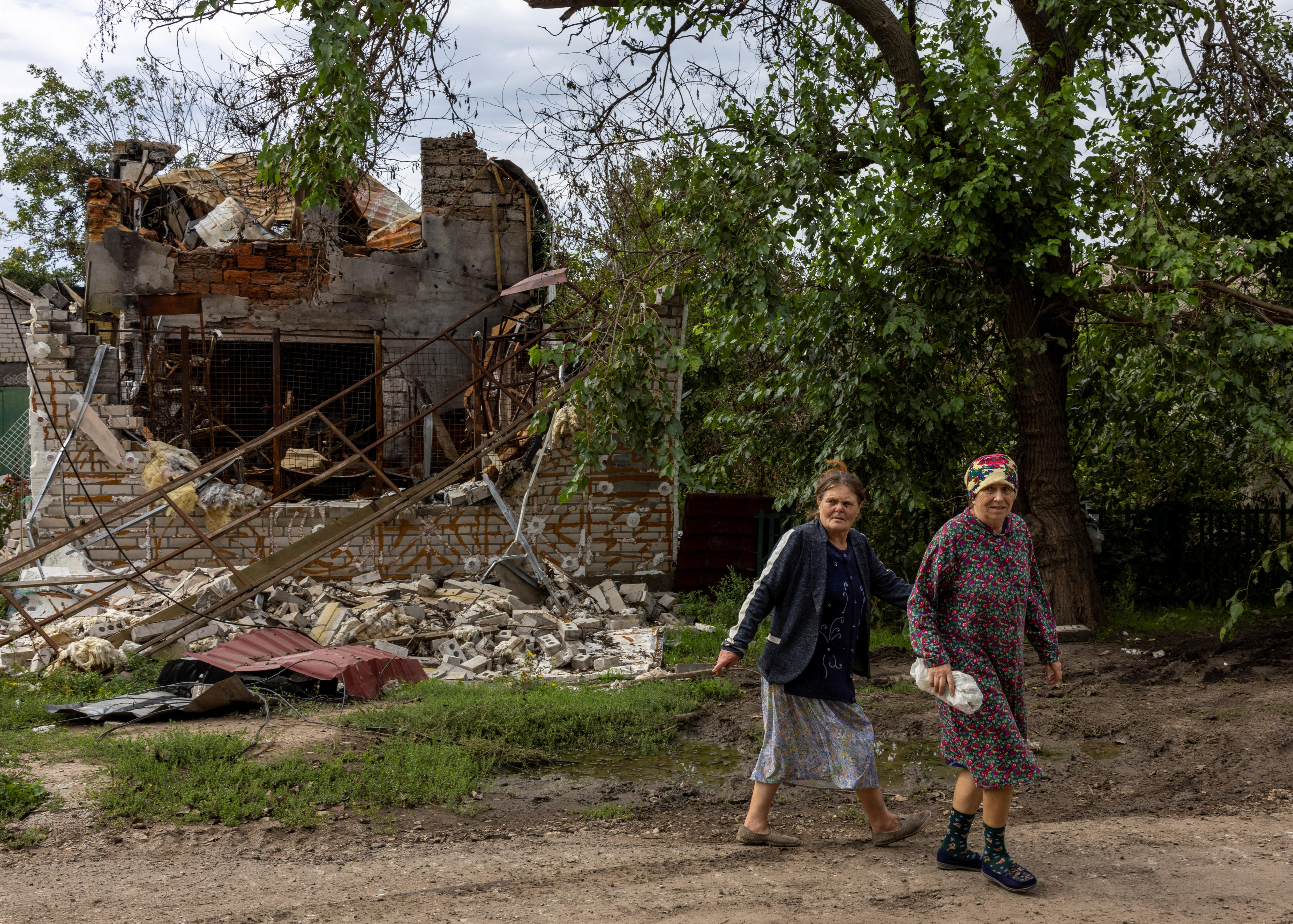 Two women walk past destroyed house.