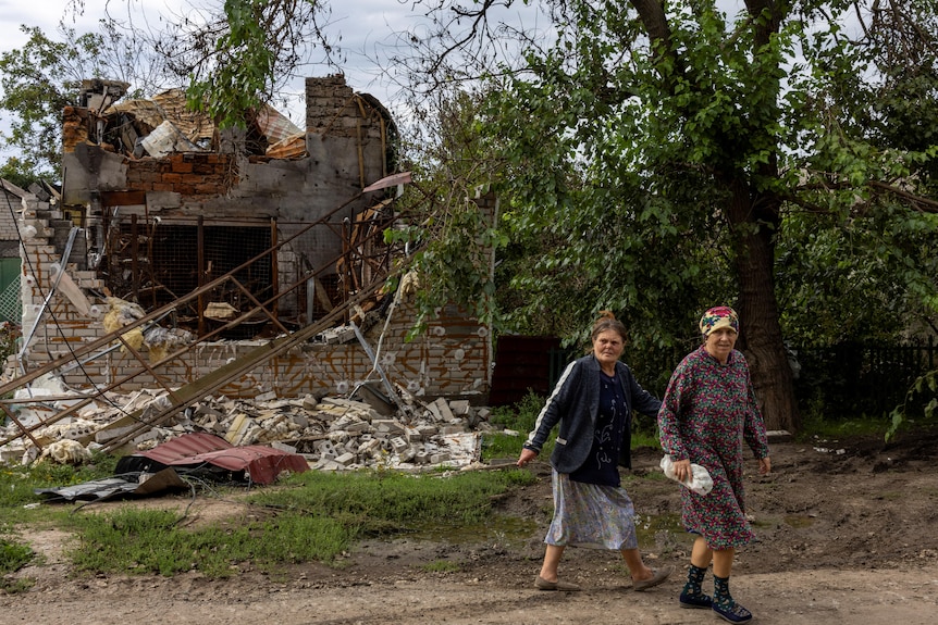 Two women walk past destroyed house.