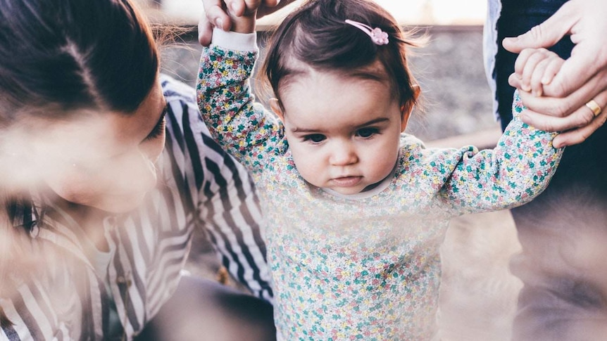 a mother holds a baby as it walks