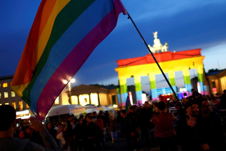 People stand in front of Brandenburg gate, lit up in rainbow colours