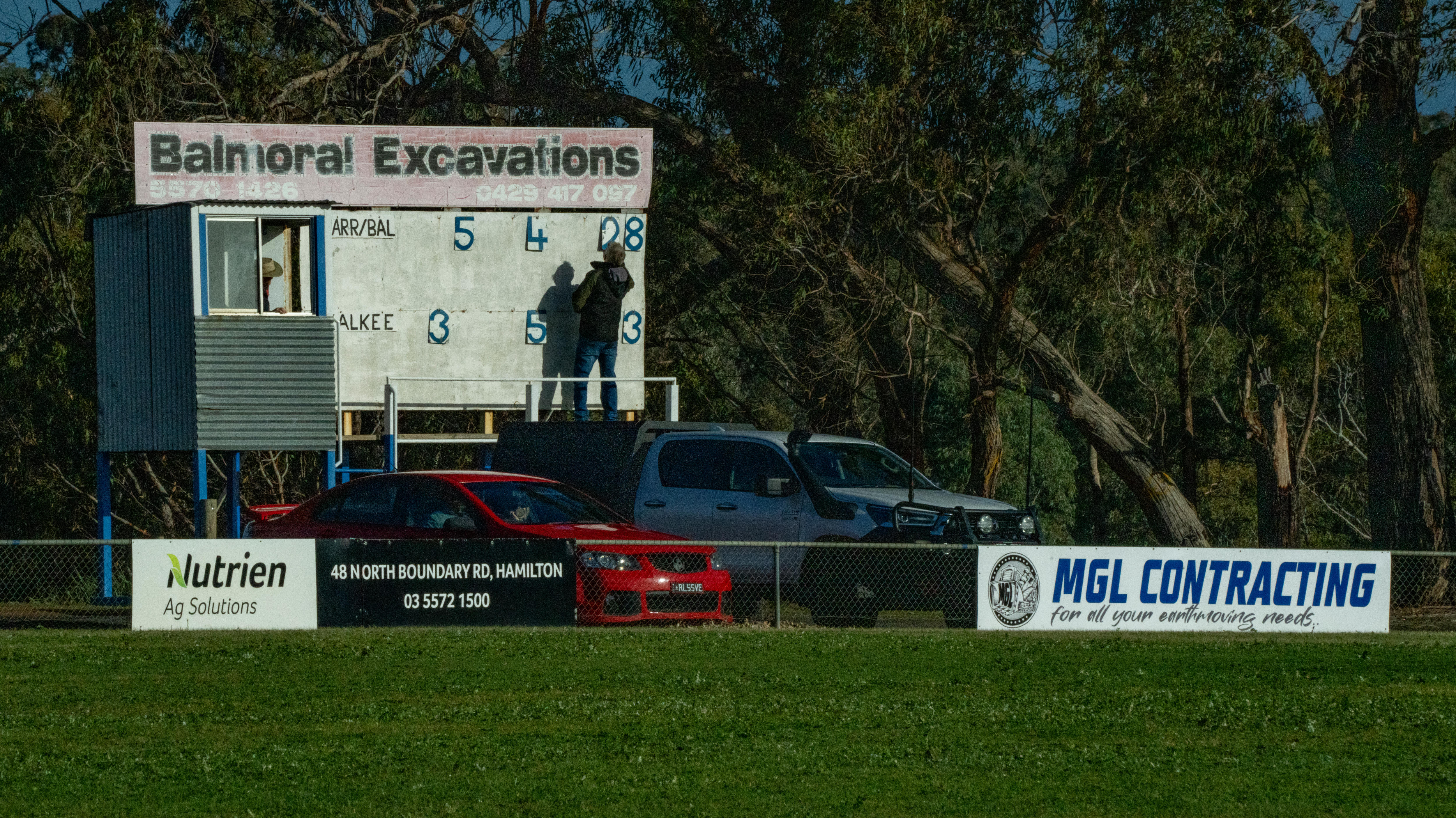 A scoreboard at a country football oval, with a man flipping the numbers.