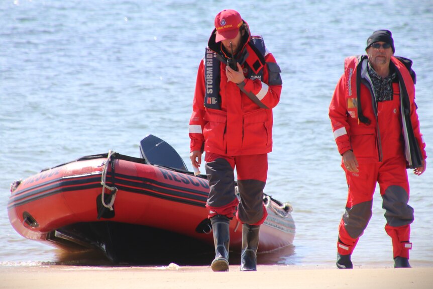 Two members of a marine rescue crew and their dinghy on a shoreline.