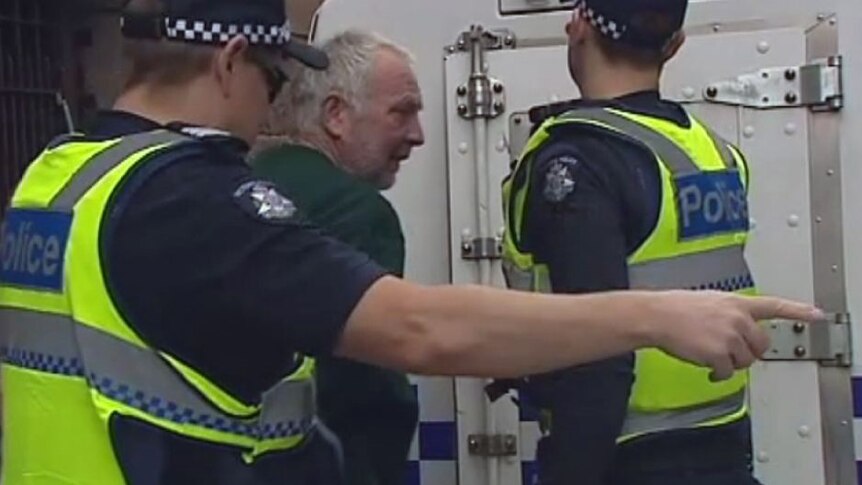 A grey haired man gets put into a police van by two police officers.