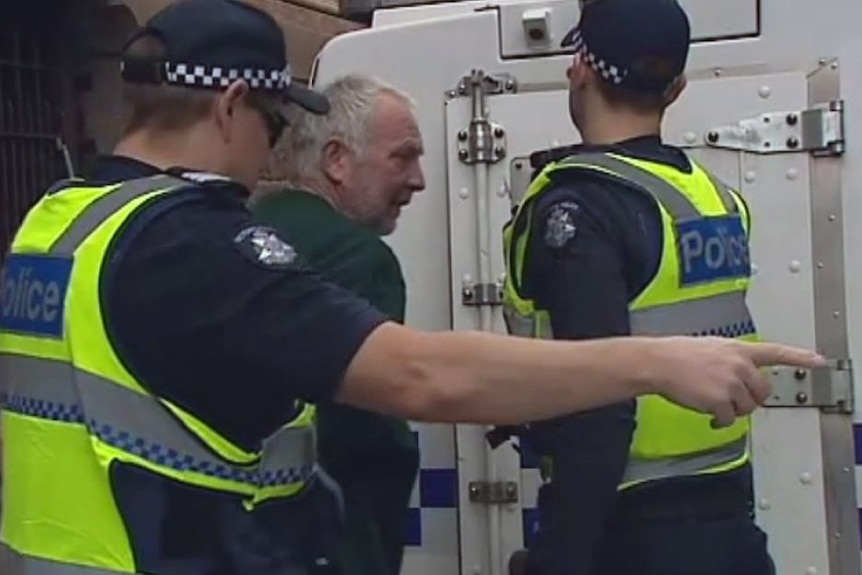 A grey haired man gets put into a police van by two police officers.