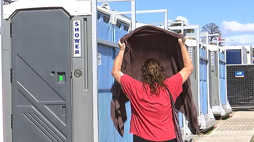 A woman with a towel in front of portable shower stalls.