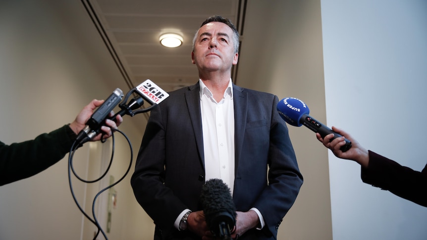 Darren Chester in a suit standing in front of microphones during a press conference