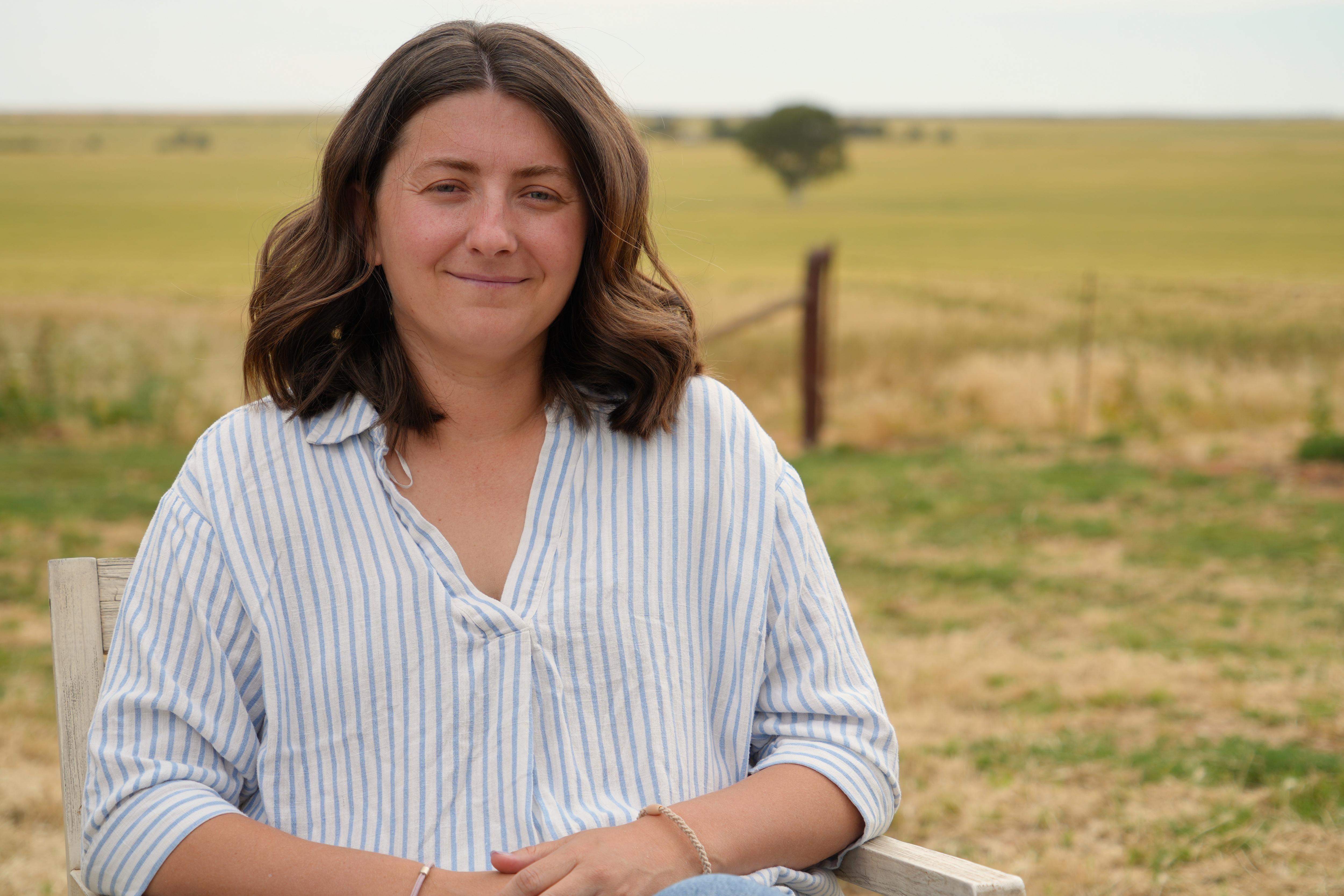 a woman sits on a chair in a paddock smiling 