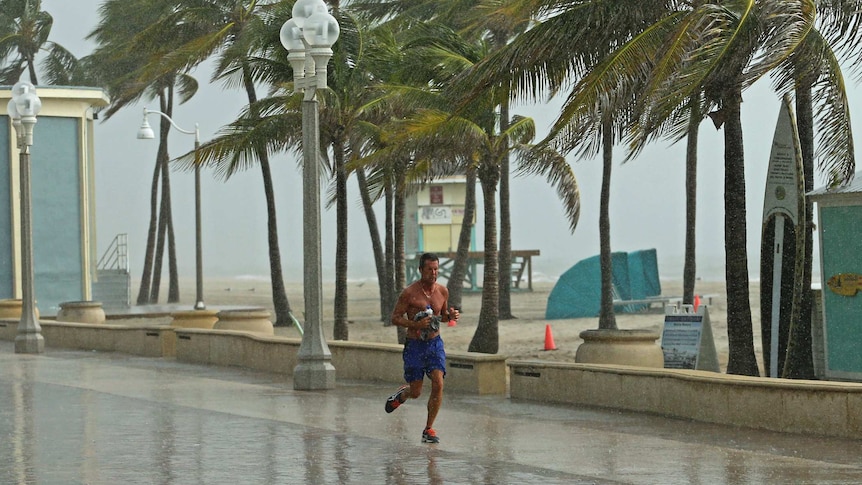 Man jogs alongside beach as huge winds and rain lashes him and area