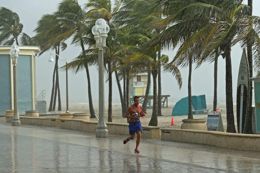 Man jogs alongside beach as huge winds and rain lashes him and area