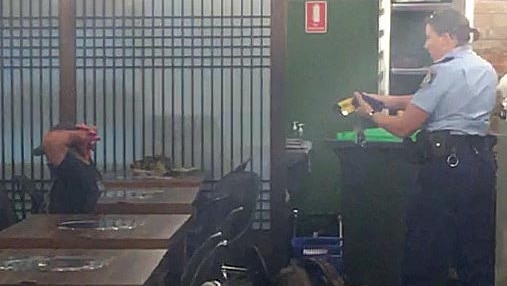 A policewoman points a taser at a man with his hands behind his head in a restaurant.