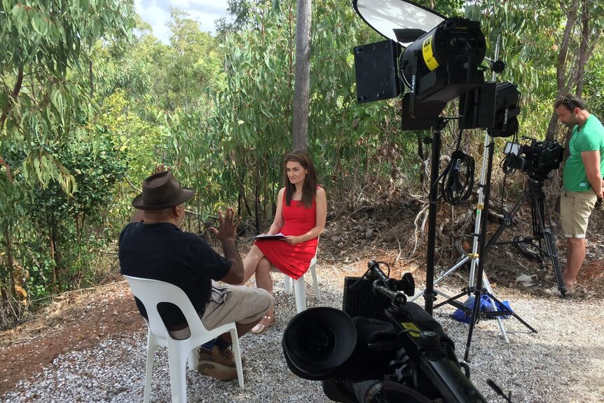 Karvelas in bush doing interview with cameraman filming and lights set up.