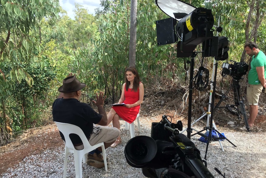 Karvelas in bush doing interview with cameraman filming and lights set up.