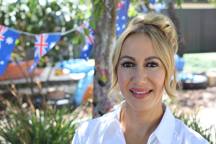 A woman in a white shirt stands in a park with Australian flag bunting behind her.
