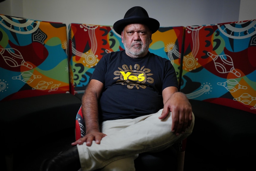 Indigenous man Noel Pearson sits in front of artwork, wearing a 'yes' t-shirt