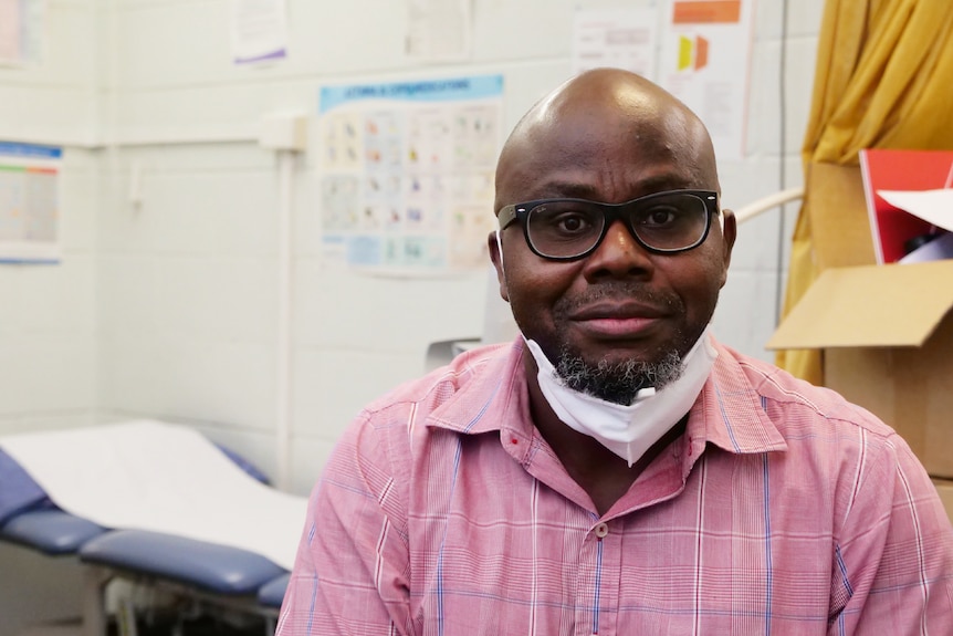 Man in glasses wearing a face mask under his chin in a doctor's office.