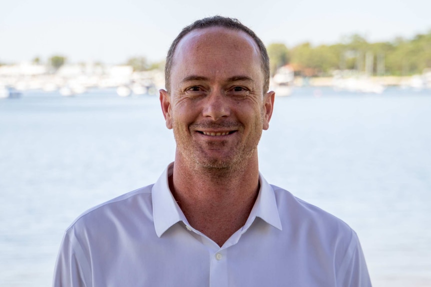 A headshot of a smiling Griffin Longley with a river and boats in the background.