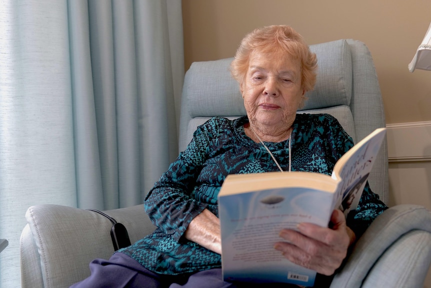 93-year-old Muriel Wilkinson sitting in an armchair and reading a book.