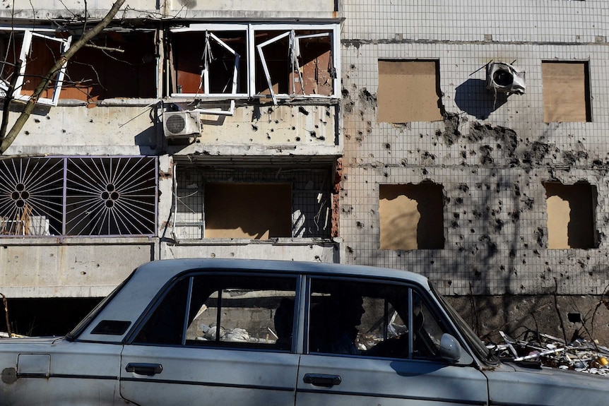 A man drives a car in front of a damaged building in Donetsk