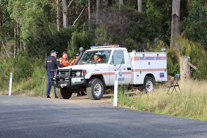 A police officer talks to SES crew in a car on a dirt road.