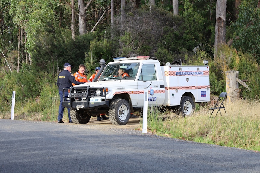 A police officer talks to SES crew in a car on a dirt road.