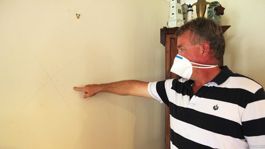 A man wearing a face mask points to a wall where a marker for toxic mould is placed