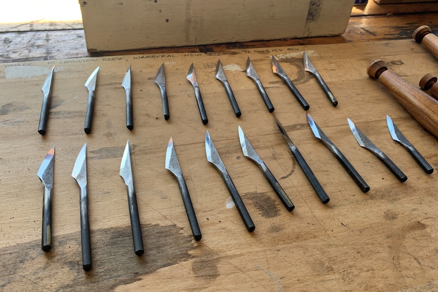 Nineteen metal blades on a bench ready to be inserted in wooden handles.