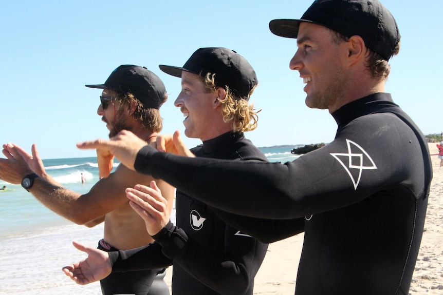 Close-up of three men standing on a beach clapping.