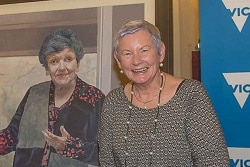 Kay Setches smiles in front of a portrait of Joan Kirner.
