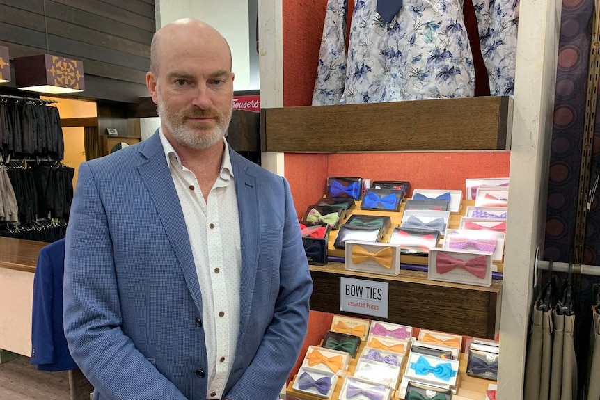 A man stands in front of a stand of bow ties in a menswear shop.