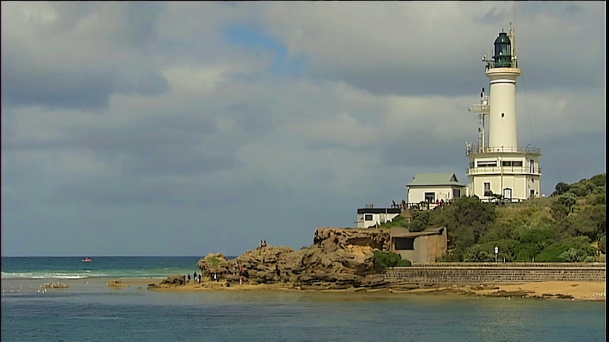 A photograph from the shore with lighthouse at right, coastline and bay view.