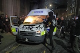 Protesters set fire to a vandalised police van and a man in a hoodie swings a chair into the vehicle's windscreen.