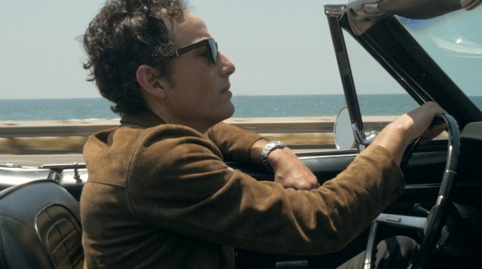 Jakob Dylan drives a convertible car by the ocean