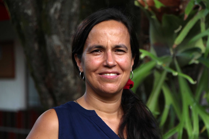 A woman smiling at the camera with trees behind her