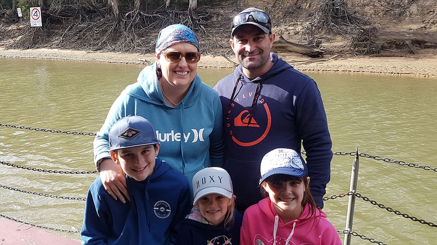 Mum, dad and three kids look at camera. They are standing on a platform above a riverbank.