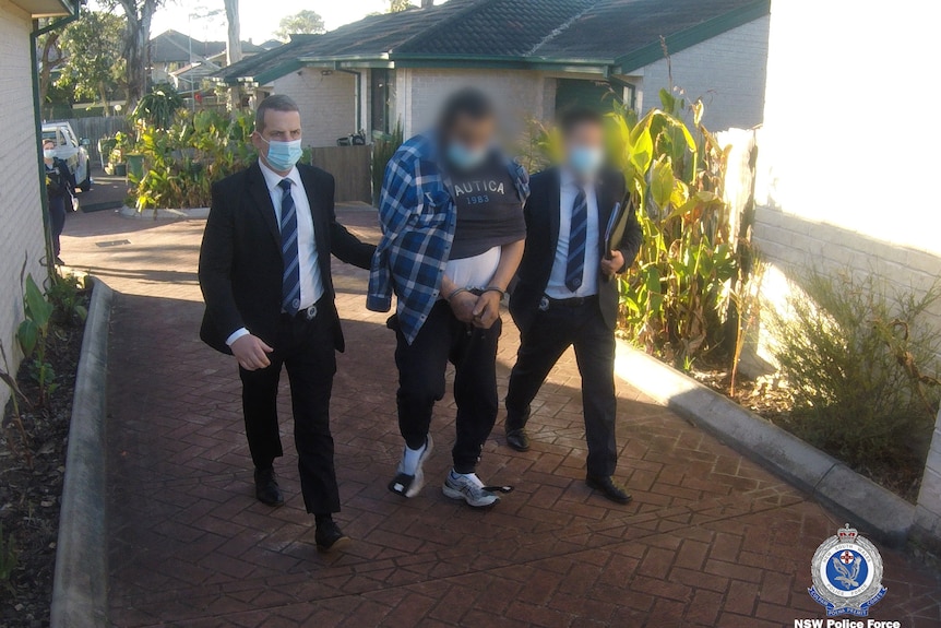 A man with handcuffs walking between two men in suits 
