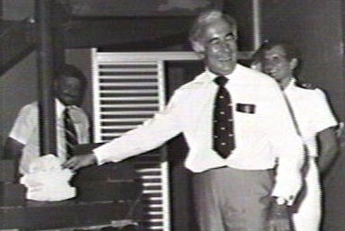 Blurred black and white of man in suit smiling and holding something posing for onlookers