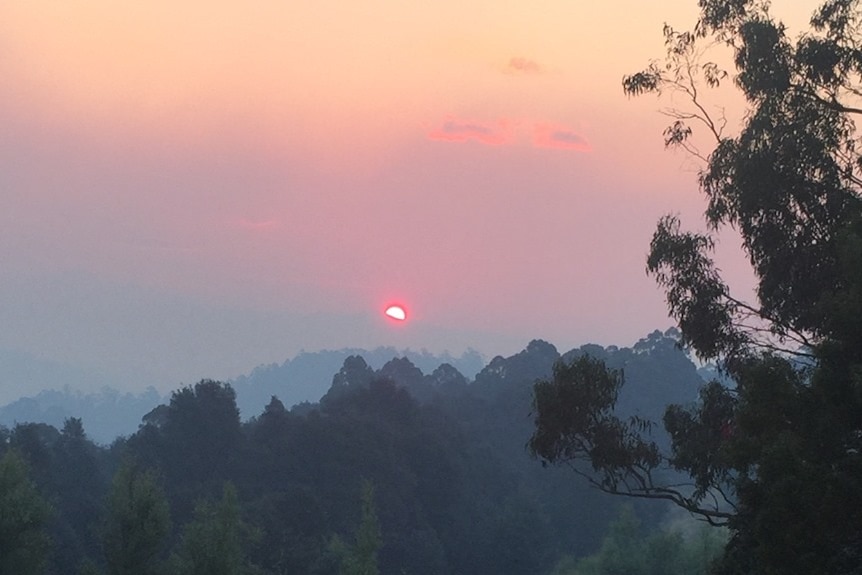 A picture of a sunset on a mountain with thick smoke in the air.